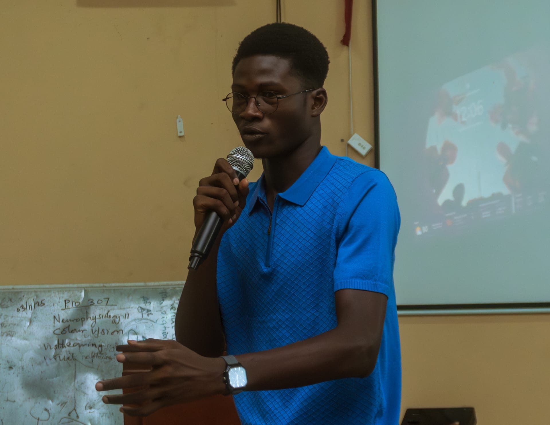 Abdul-Salam speaking into a microphone in front of a projector screen