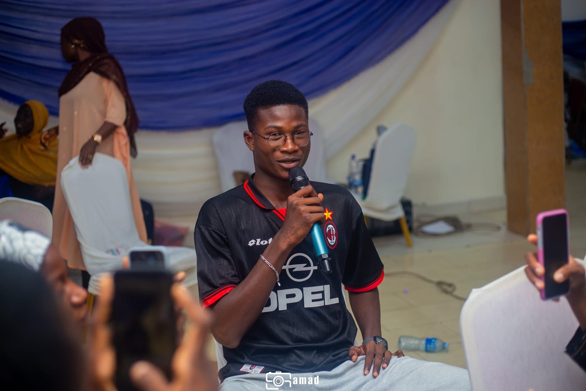 Abdul-Salam seated with a microphone, addressing an audience at a community event
